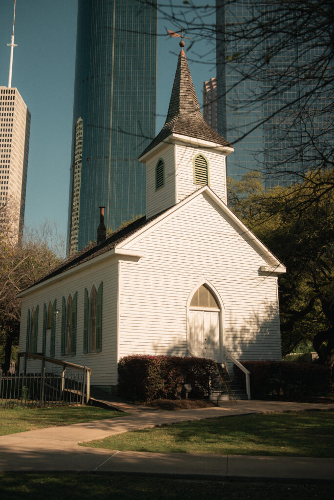 Historic white chapel exterior in Houston with downtown buildings in the background.