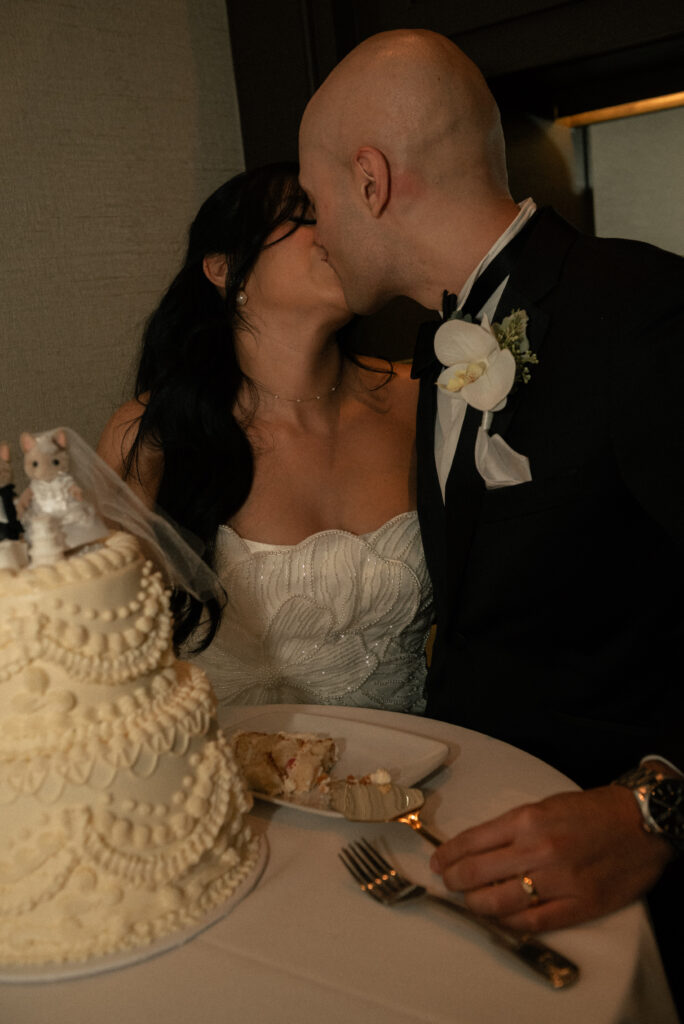 Couple kissing during cake cutting at the wedding reception.