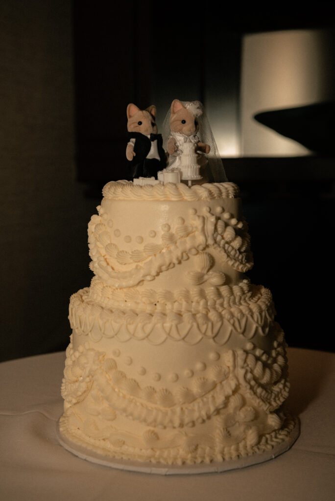 Wedding cake detail with vintage-style piping and a cute topper in low light.