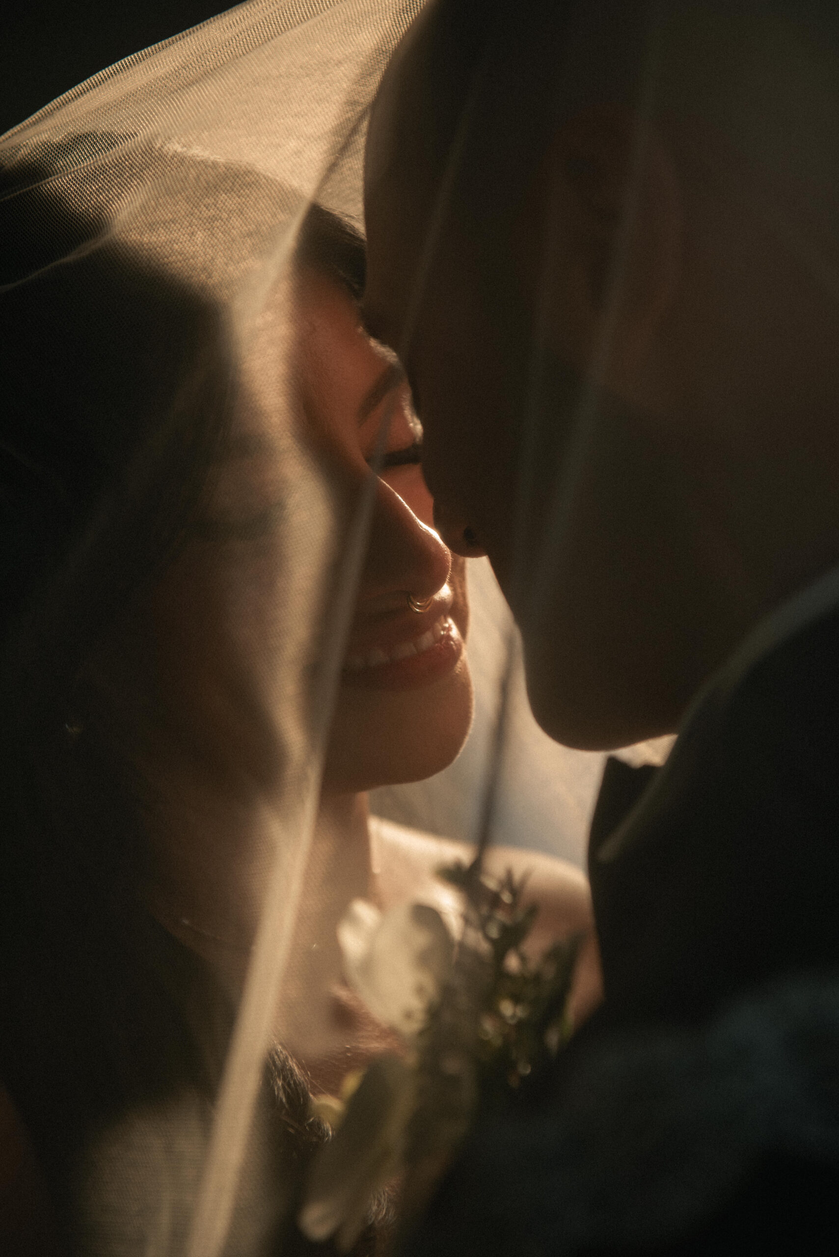 Intimate couple portrait under veil with soft golden light and close framing.