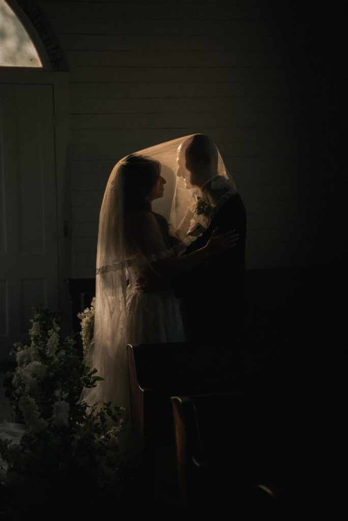 Romantic silhouette of couple under veil with warm backlight in a quiet moment.