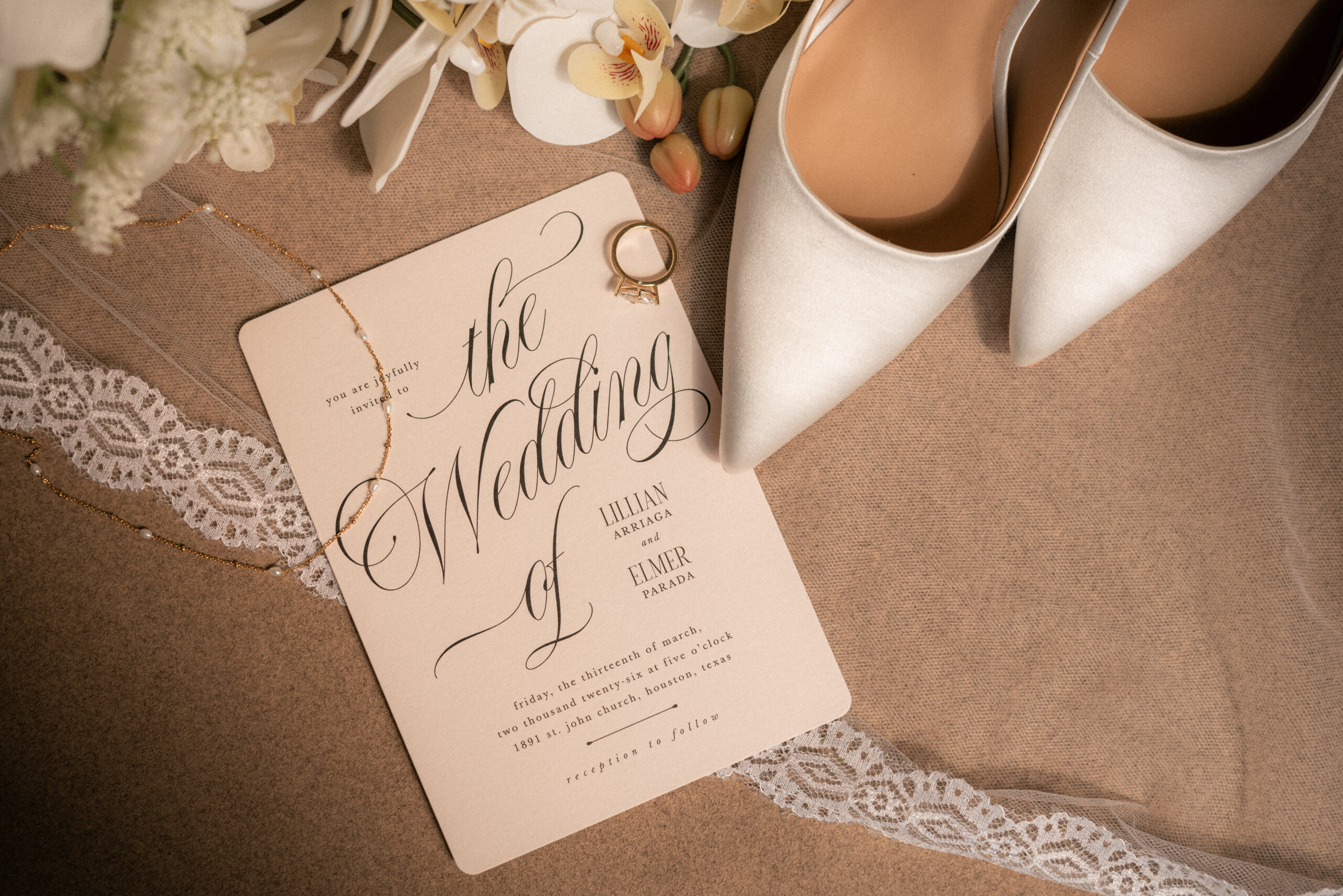 Wedding flat lay with invitation suite, rings, and bridal shoes on neutral fabric.