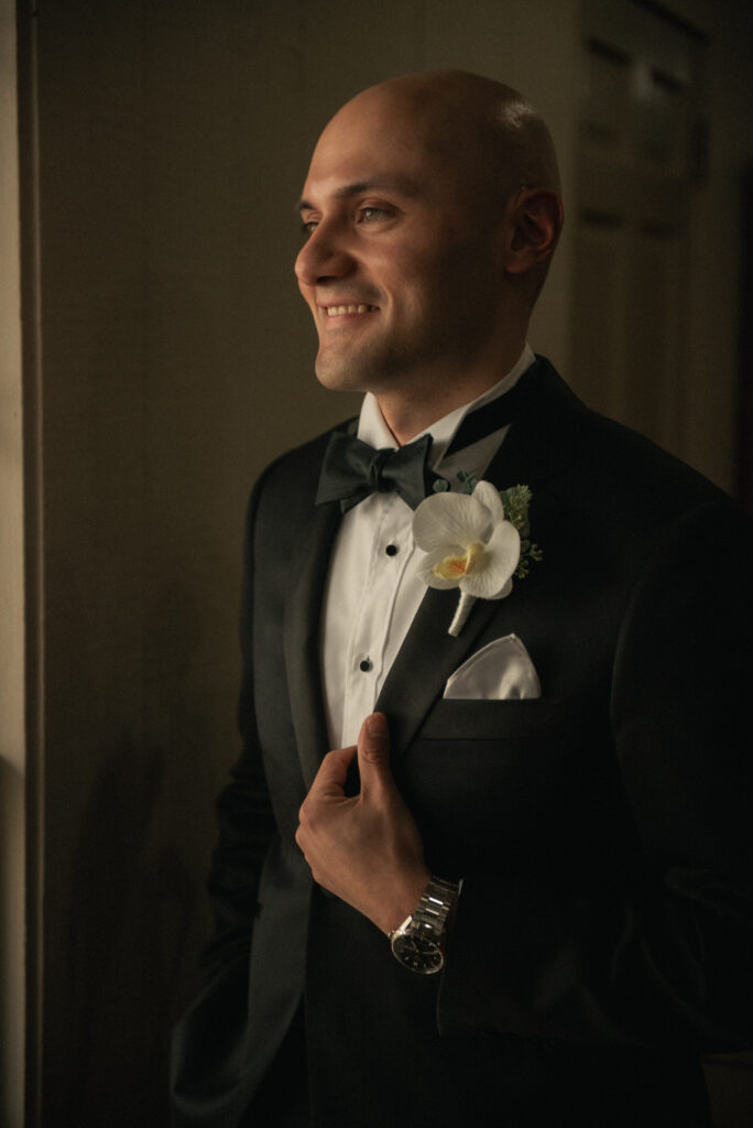 Groom portrait in tux standing by window light before the ceremony.