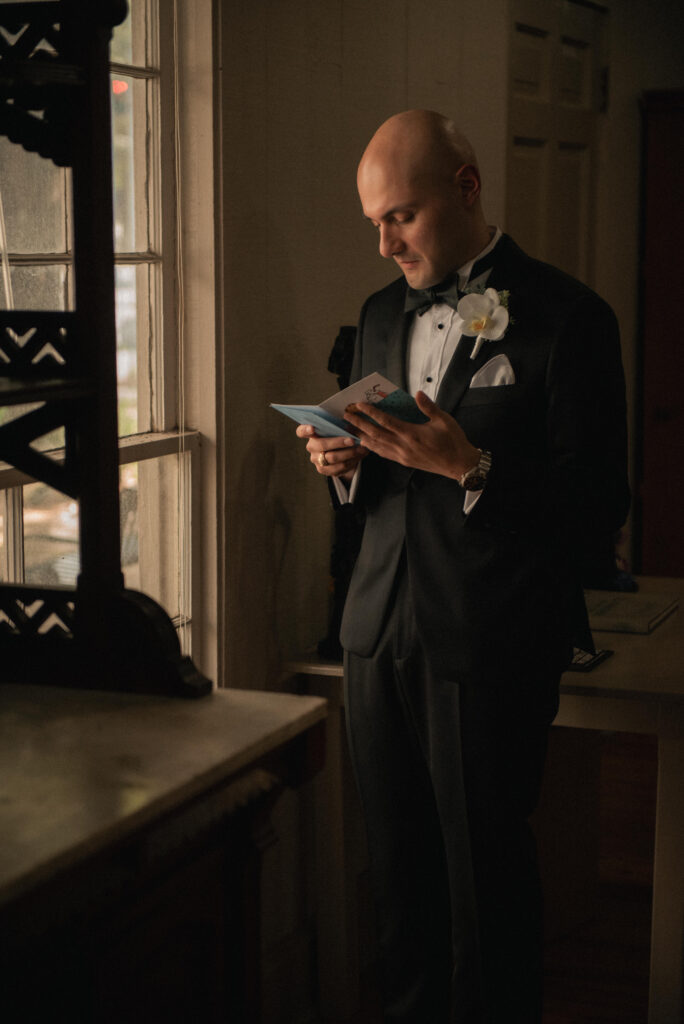 Groom reading a letter by a window during wedding day getting ready.