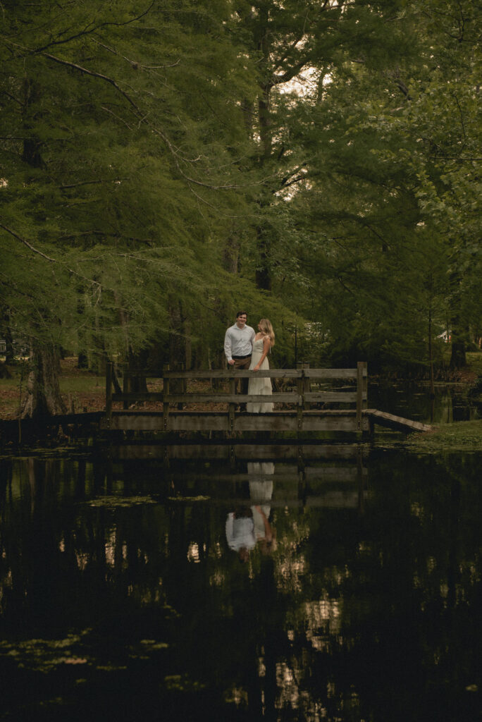 Couple standing on a bridge with water reflection during a Houston engagement session.