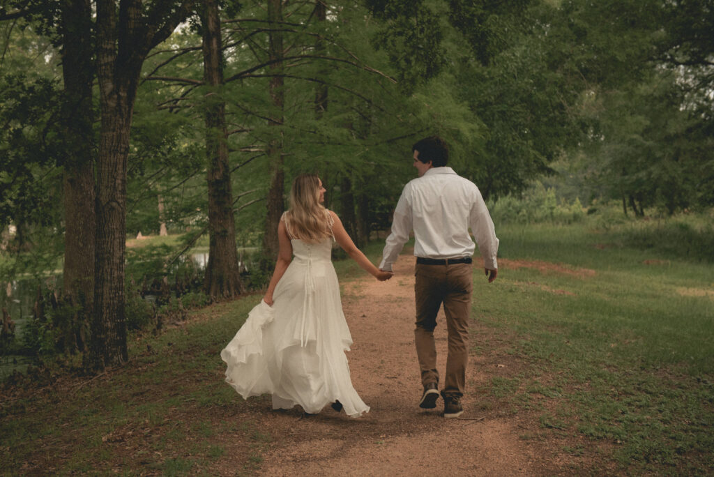 Engaged couple walking hand in hand down a wooded trail in a Houston park.