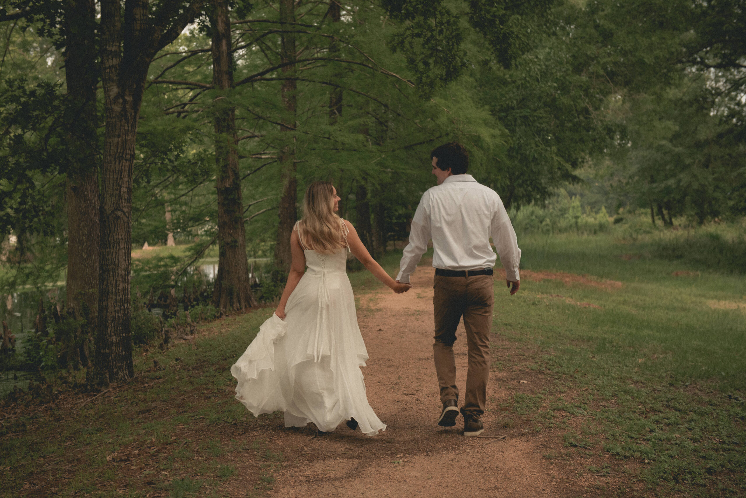Engaged couple walking hand in hand down a wooded trail in a Houston park.