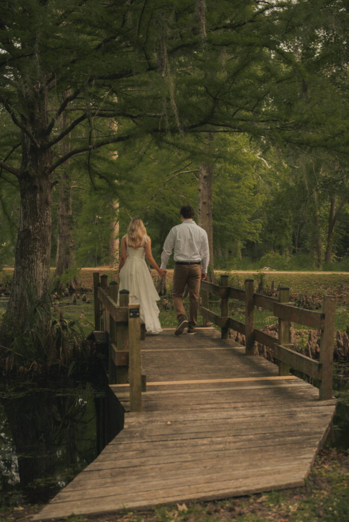 Engaged couple walking on a wooden bridge in a wooded Houston park.