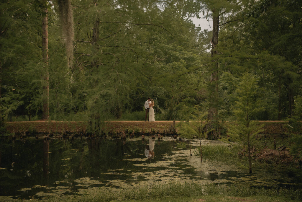 Wide shot of an engaged couple near a pond with reflections in a Houston park.